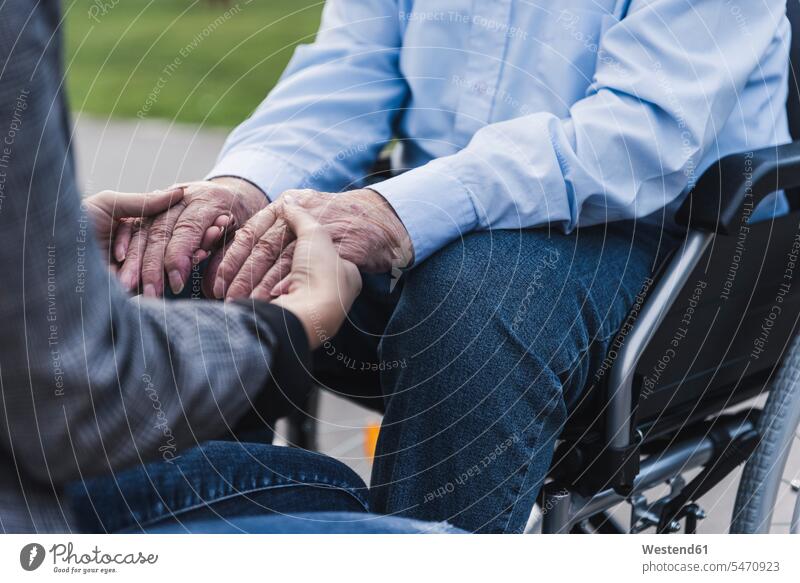 Junge Frau hält Hände eines älteren Mannes, der im Rollstuhl sitzt, Teilansicht Generation anfassen Berührung sitzend gefühlvoll Emotionen Empfindung