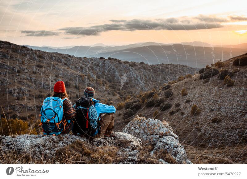 Männliche und weibliche Wanderer genießen den Sonnenuntergang, während sie im Urlaub auf dem Felsenberg sitzen Farbaufnahme Farbe Farbfoto Farbphoto