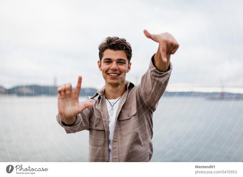 Lächelnder junger Mann zeigt Handzeichen gegen den Himmel Farbaufnahme Farbe Farbfoto Farbphoto Portugal Außenaufnahme außen draußen im Freien Tag