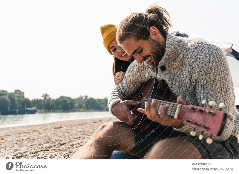 Glückliches junges Paar mit Gitarre am Flussufer Gitarren Pärchen Paare Partnerschaft glücklich glücklich sein glücklichsein Saiteninstrument Saiteninstrumente