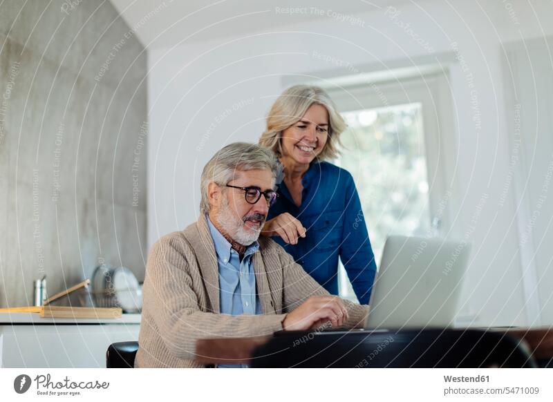 Reifer Mann mit Frau, der zu Hause einen Laptop auf dem Küchentisch benutzt Leute Menschen People Person Personen Europäisch Kaukasier kaukasisch 2 2 Menschen
