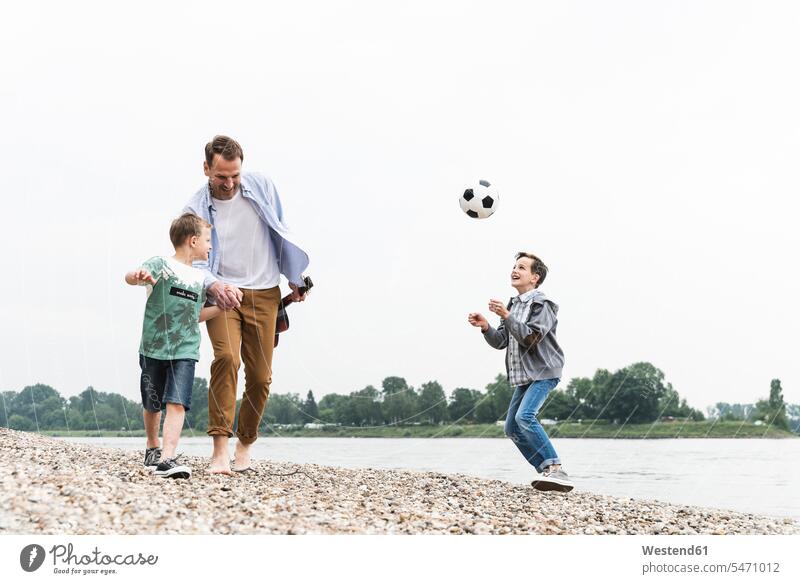 Glücklicher Vater mit zwei Söhnen und Fussball am Flussufer Fußball Fußbälle Sohn Papas Väter Vati Vatis Papis gehen gehend geht glücklich glücklich sein