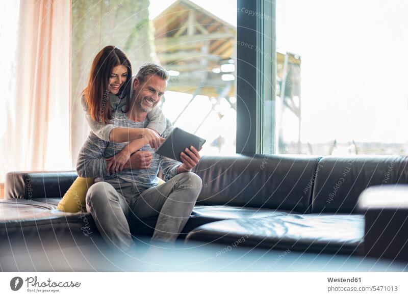 Glückliches Paar auf der Couch zu Hause, das sich eine Tablette teilt Sofa Couches Liege Sofas glücklich glücklich sein glücklichsein Teilen Sharing Pärchen