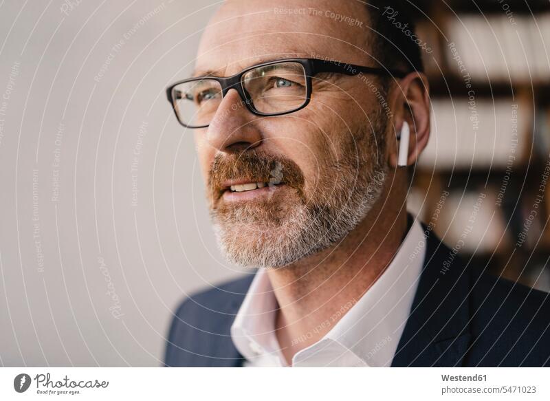 Porträt eines reifen Geschäftsmannes, der mit Bluetooth-Kopfhörern Musik hört Leute Menschen People Person Personen Europäisch Kaukasier kaukasisch erwachsen