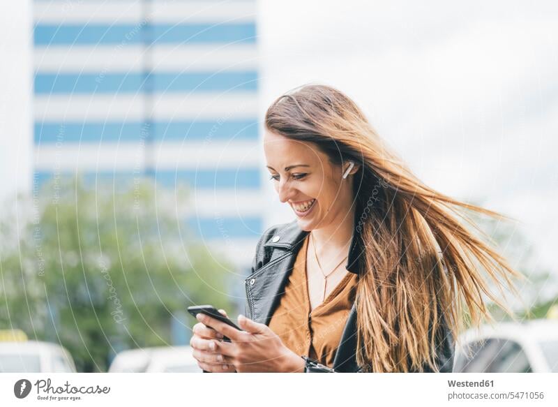 Glückliche junge Frau mit windgepeitschtem Haar beim Telefonieren in der Stadt Handy Mobiltelefon Handies Handys Mobiltelefone wehen wehend glücklich