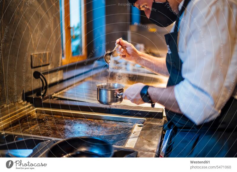 Koch mit Gesichtsschutz bei der Zubereitung einer Sauce in der Restaurantküche Leute Menschen People Person Personen Europäisch Kaukasier kaukasisch 1 Ein