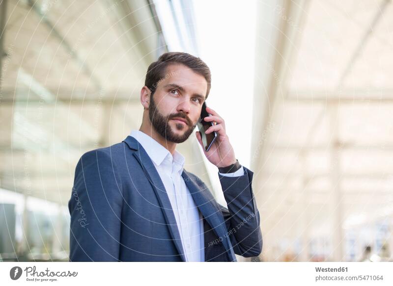Junger Geschäftsmann am Handy schaut seitwärts Businessmann Businessmänner Geschäftsmänner telefonieren anrufen Anruf telephonieren Mobiltelefon Handies Handys