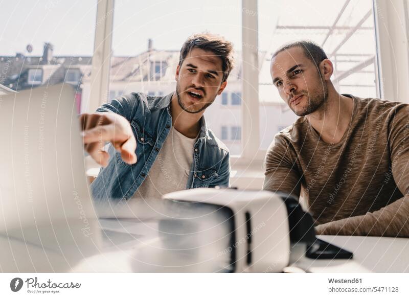 Zwei junge Geschäftsmänner betrachten Laptop mit VR-Brille auf dem Schreibtisch Job Berufe Berufstätigkeit Beschäftigung Jobs Rechner Laptops Notebook Notebooks