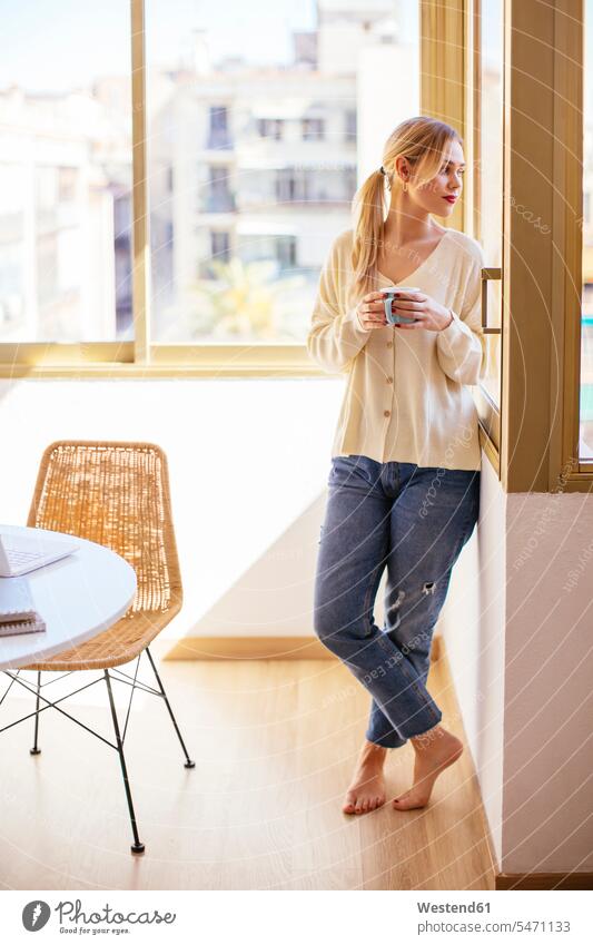 Blonde Frau mit einer Tasse Kaffee, die aus dem Fenster schaut weiblich Frauen blond blonde Haare blondes Haar aus dem Fenster sehen durchs Fenster schauen