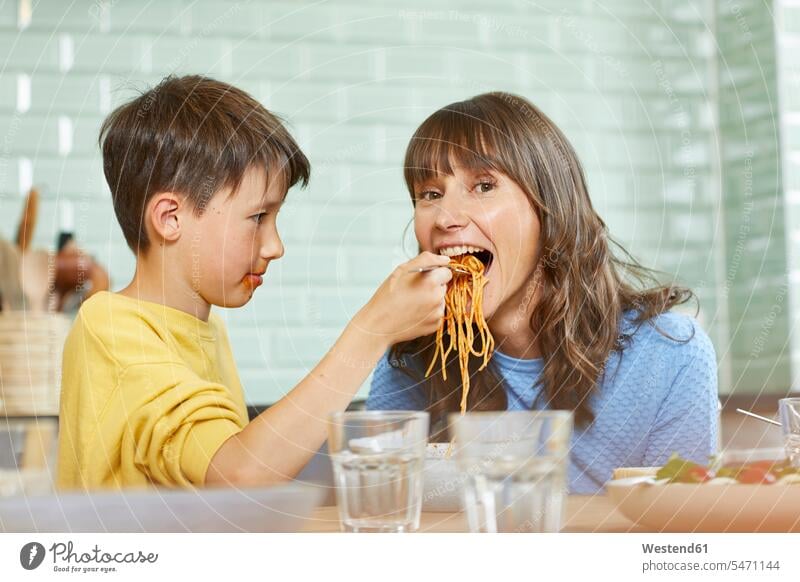 Sohn füttert Mutter mit Spaghetti in der Küche sitzend sitzt freuen Frohsinn Fröhlichkeit Heiterkeit Glück glücklich sein glücklichsein daheim zu Hause