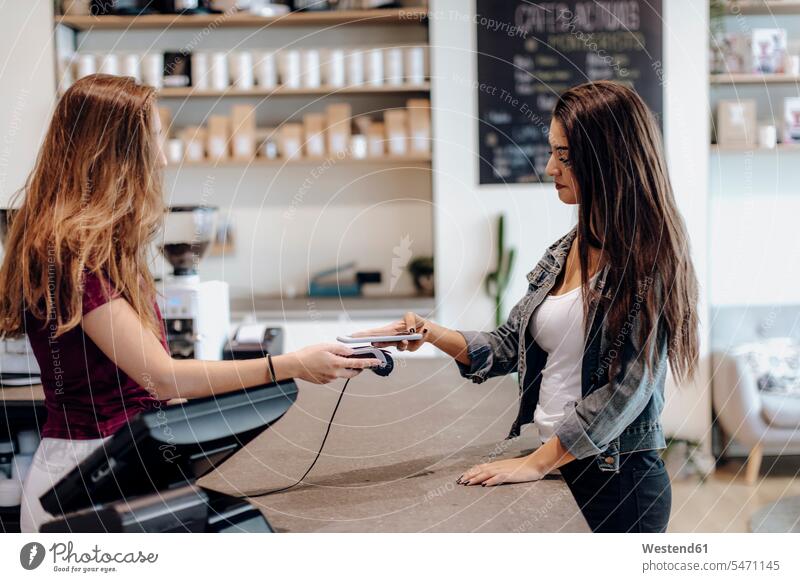 Junge Frau bezahlt bargeldlos mit Smartphone an der Theke eines Cafés Spanien iPhone Smartphones Kartenlesegerät Kartenlesegeraet gegenüber gegenueber Lifestyle