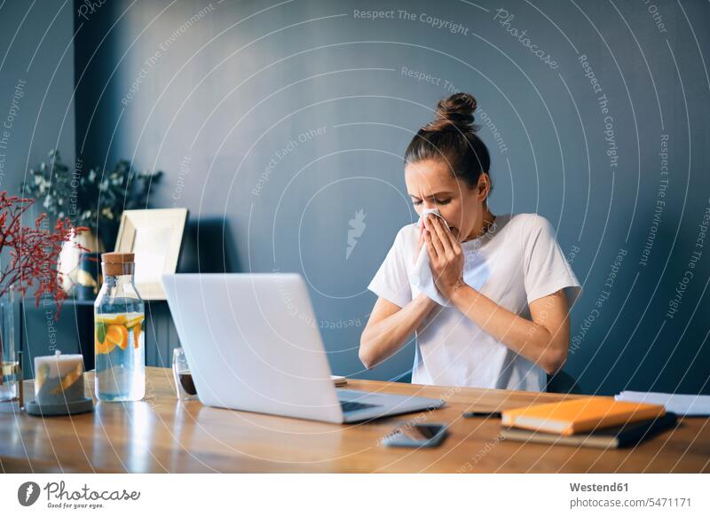 Geschäftsfrau putzt sich die Nase, während sie im Heimbüro am Schreibtisch sitzt Farbaufnahme Farbe Farbfoto Farbphoto Freizeitkleidung Freizeitbekleidung