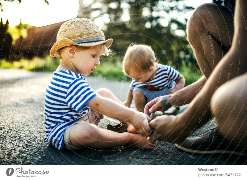 Vater hilft seinem kleinen Sohn beim Ausziehen der Schuhe Papas Väter Vati Vatis Papis Söhne helfen mithelfen Hilfsbereitschaft beistehen Mithilfe Beistand