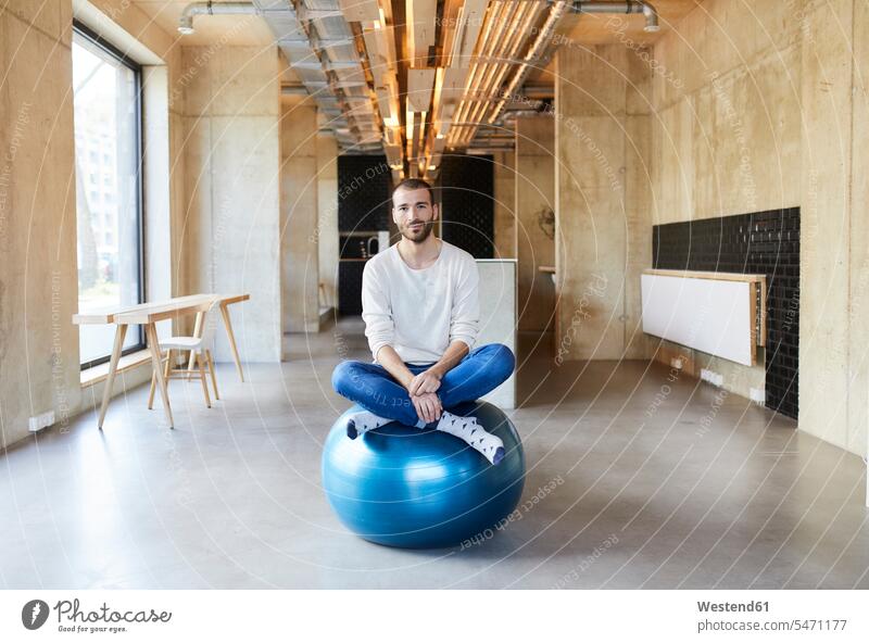 Porträt eines jungen Mannes, der auf einem Fitnessball in einem modernen Büro sitzt Europäer Kaukasier Europäisch kaukasisch Körperhaltung Haltung