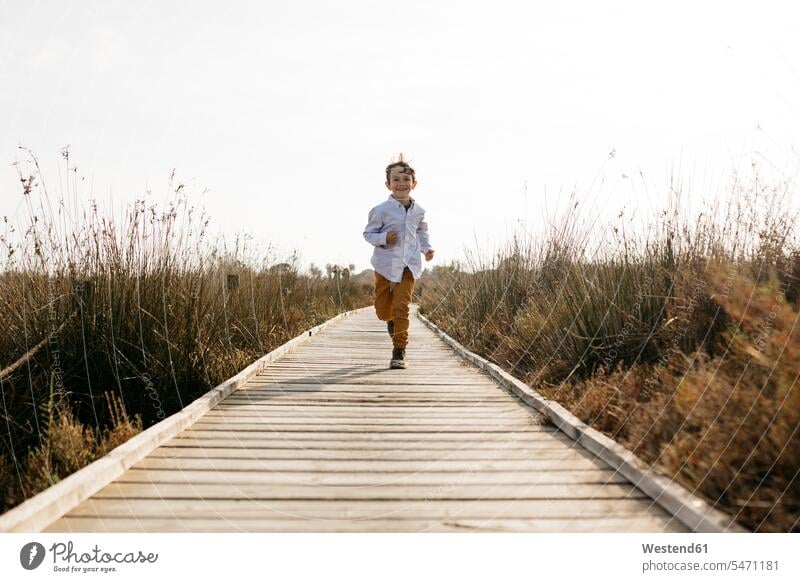 Glücklicher kleiner Junge, der auf der Strandpromenade läuft Europäer Kaukasier Europäisch kaukasisch Vorderansicht frontal von vorne Frontalansicht