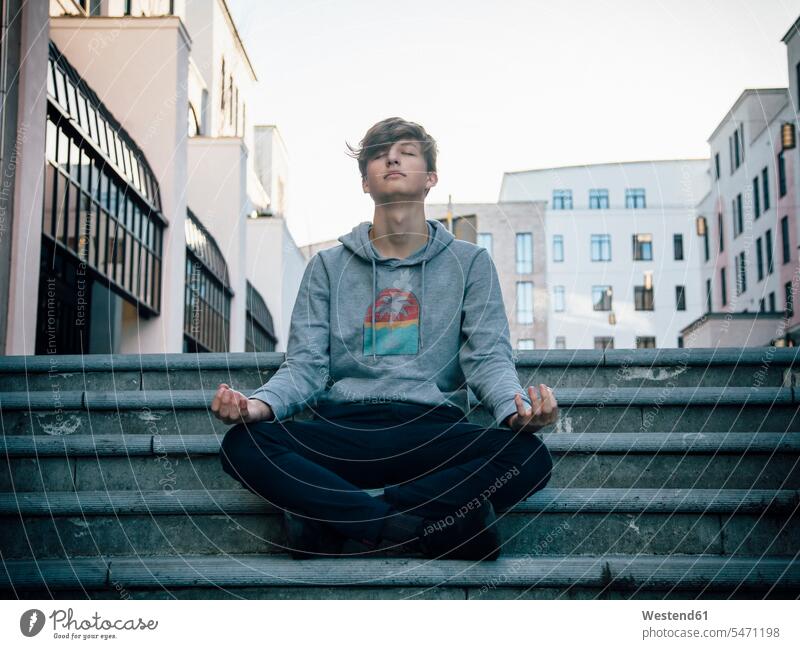 Teenager sitzt auf Stufen und meditiert in der Stadt Kopfhoerer entspannen relaxen sitzend Glück glücklich sein glücklichsein zufrieden Muße Lifestyles
