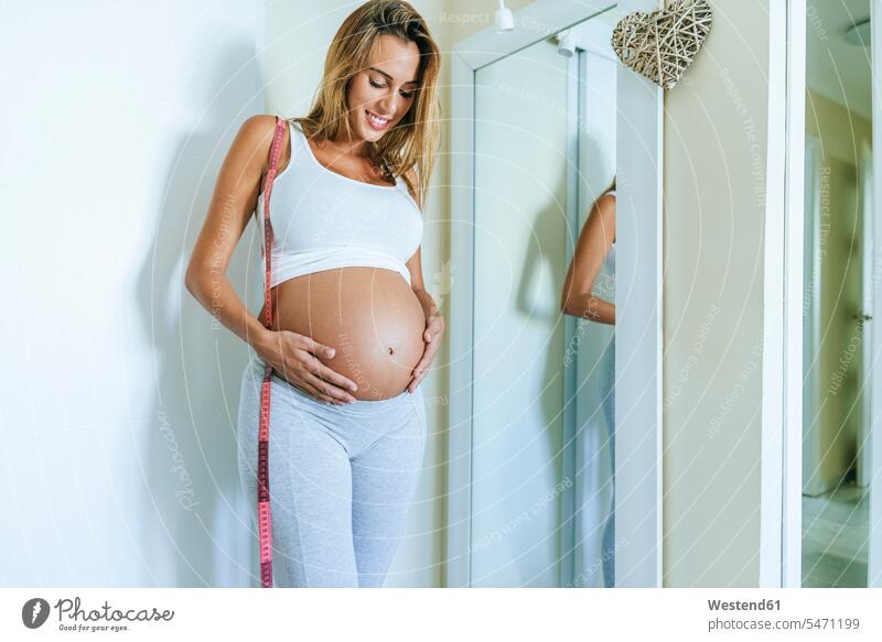 Schwangere Frau schaut auf ihren Bauch vor dem Spiegel ansehen weiblich Frauen schwanger schwangere Frau Bäuche schauen sehend Erwachsener erwachsen Mensch