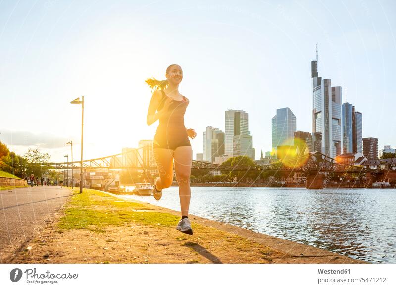 Deutschland, Hessen, Frankfurt, Junge Frau joggt bei Sonnenuntergang am Mainufer Außenaufnahme außen draußen im Freien Sonnenuntergänge Stimmung stimmungsvoll