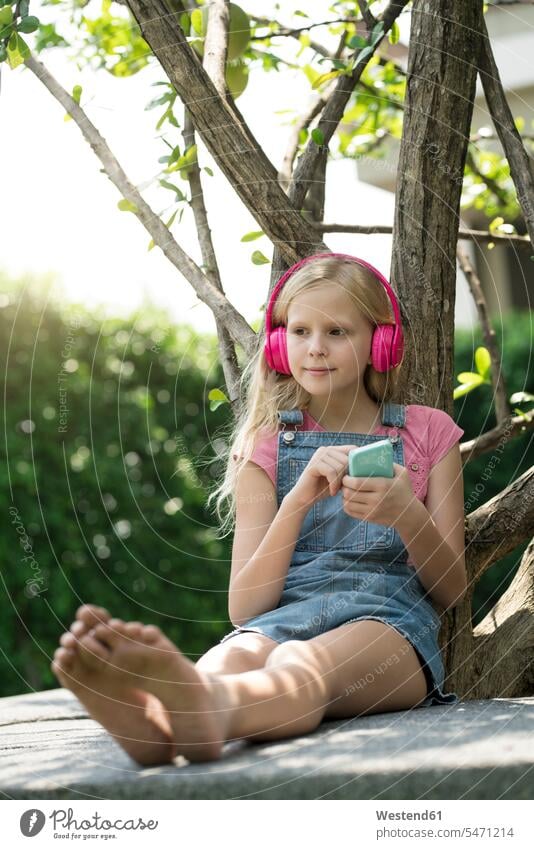 Süßes blondes Mädchen hört Musik mit rosa Kopfhörern im Garten Kopfhoerer pink pinkfarben niedlich süss süß putzig weiblich Gärten Gaerten hören hoeren Magenta