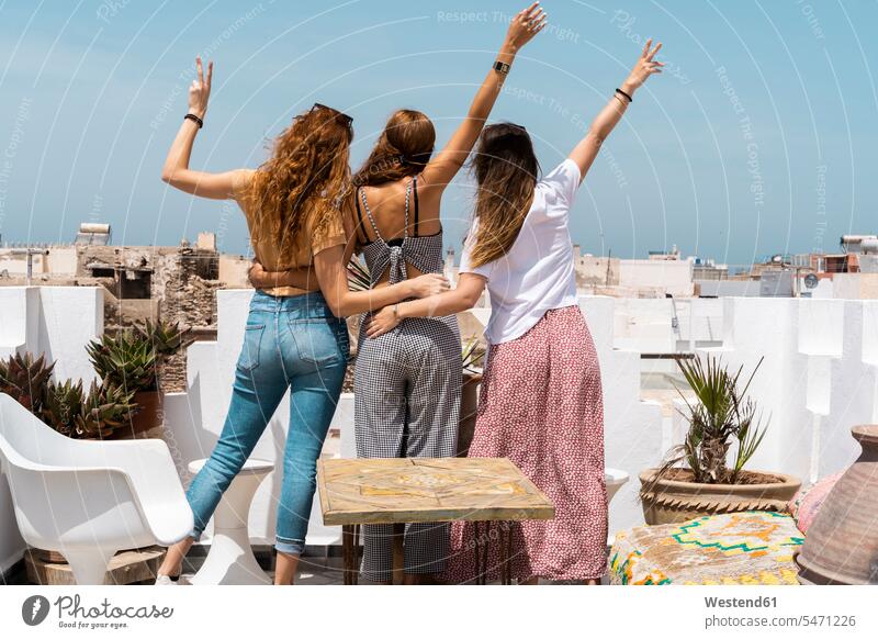 Rückansicht von drei jungen Frauen, die auf der Dachterrasse stehen und Siegeszeichen zeigen, Essaouira, Marokko Leute Menschen People Person Personen