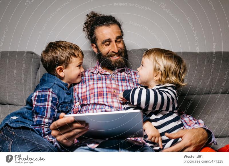 Glücklicher Vater sitzt mit seinen Kindern auf der Couch und benutzt ein digitales Tablet Väter Papa Vati Familienvater Papi Kids Tablet Computer Tablet-PC