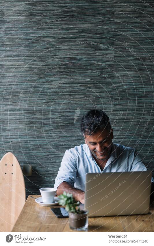 Lächelnder Gelegenheits-Geschäftsmann mit Skateboard mit Laptop in einem Cafe Job Berufe Berufstätigkeit Beschäftigung Jobs geschäftlich Geschäftsleben