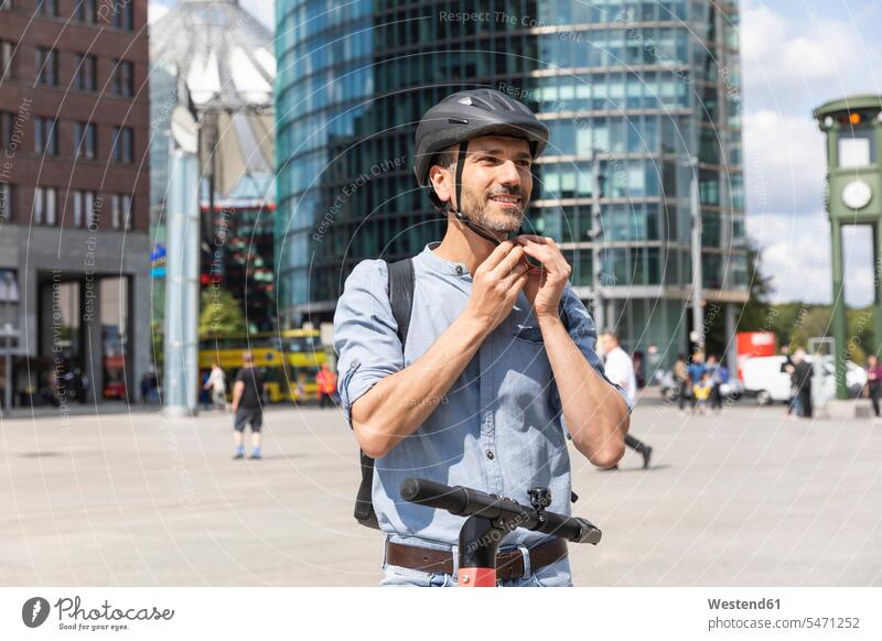 Mann befestigt den Helm, bevor er auf einem Elektroroller fährt, Berlin, Deutschland Leute Menschen People Person Personen Europäisch Kaukasier kaukasisch 1 Ein