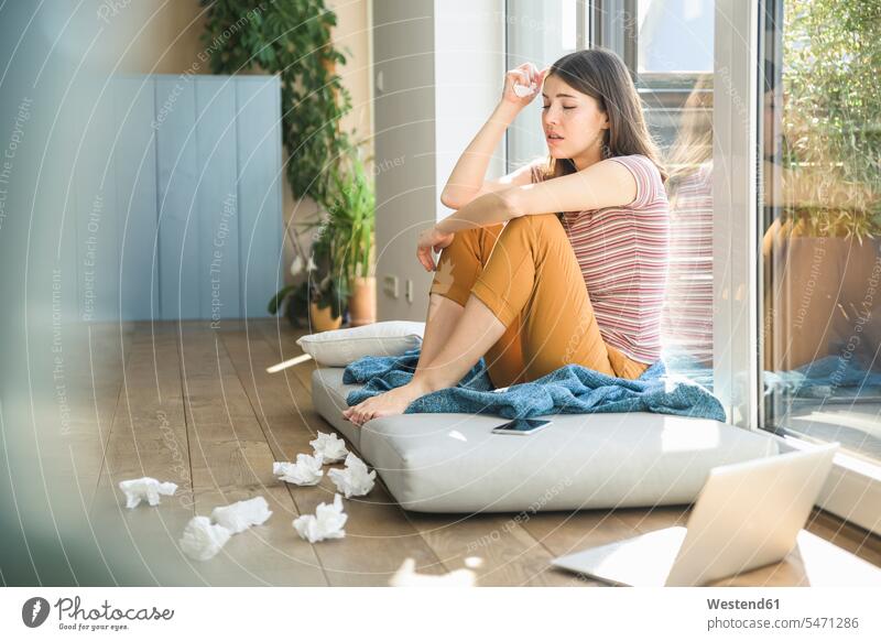 Traurige junge Frau sitzt am Fenster zu Hause mit Laptop und Taschentücher Zuhause daheim Papiertaschentuch Papiertaschentücher Taschentuch Papiertaschentuecher