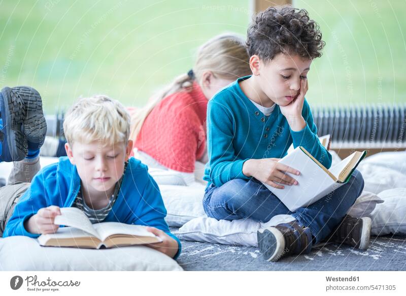 Schülerinnen und Schüler lesen Bücher auf dem Boden im Pausenraum der Schule Buch liegen liegend liegt Böden Boeden Lektüre Schulen Schulkind Schueler