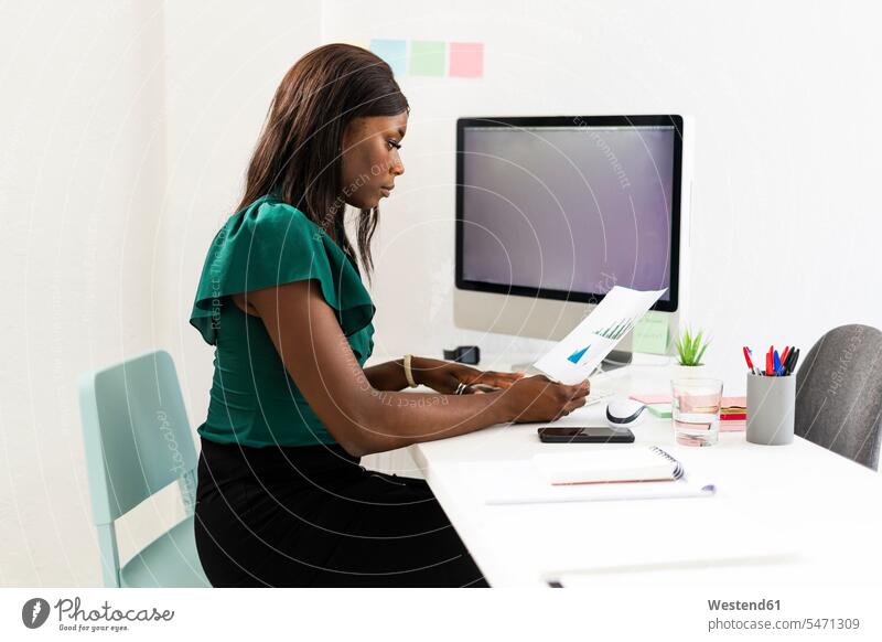 Geschäftsfrau analysiert Millimeterpapier, während sie im Büro am Schreibtisch sitzt Farbaufnahme Farbe Farbfoto Farbphoto Innenaufnahme Innenaufnahmen innen