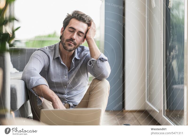 Junger Mann sitzt zu Hause auf dem Boden, mit Laptop, macht eine Pause Sofa Couches Liege Sofas Erreichbarkeit verfügbar Verfügbarkeit erreichbar Verfuegbarkeit