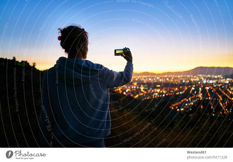 Chile, Santiago, Frau nimmt Handy-Foto in den Bergen über der Stadt bei Sonnenuntergang staedtisch städtisch Sonnenuntergänge Mobiltelefon Handies Handys
