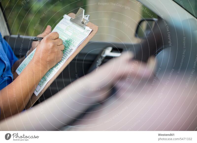 Nahaufnahme des Inspektors beim Schreiben des Testskripts im Auto schreiben aufschreiben notieren schreibend Schrift Fahrlehrer Fahrschullehrer Prüfer Wagen