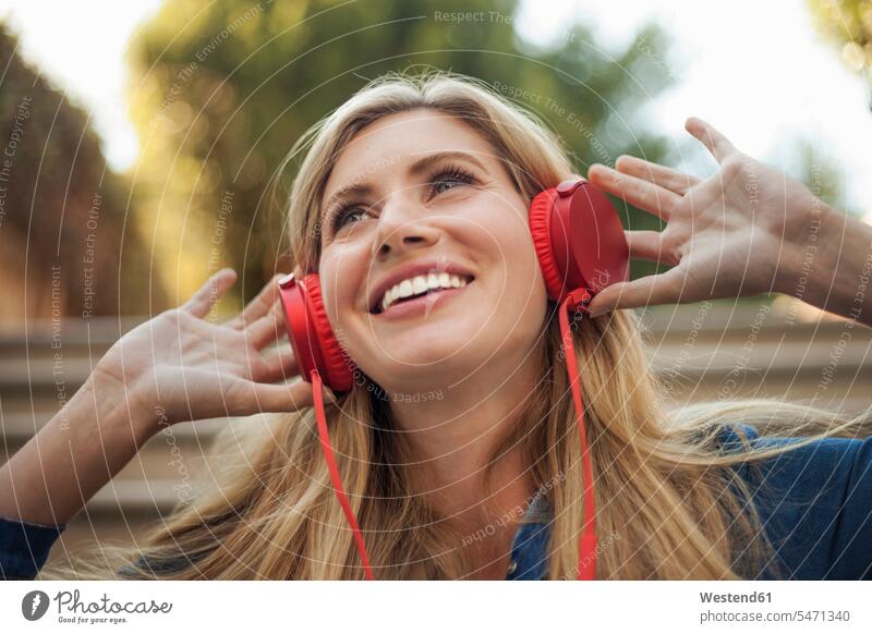 Porträt einer lächelnden Frau, die mit roten Kopfhörern Musik hört Leute Menschen People Person Personen Europäisch Kaukasier kaukasisch 1 Ein ein Mensch