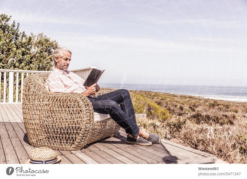 Mann liest ein Buch auf einem Deck an der Küste Touristen Bücher Hemden Lektüre sitzend sitzt Jahreszeiten sommerlich Sommerzeit entspannen relaxen