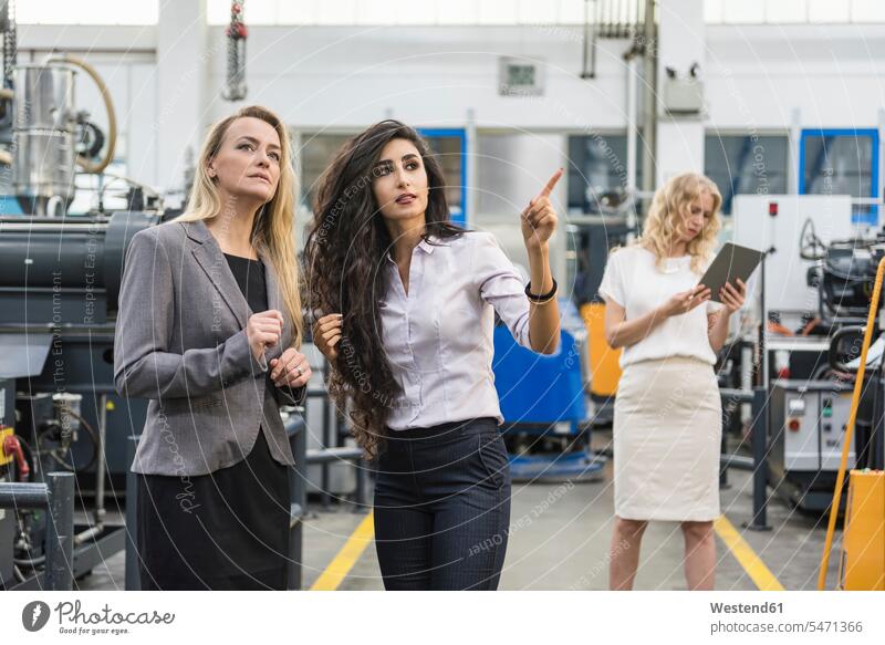 Zwei Frauen unterhalten sich in einer Fabrikhalle mit einer Frau im Hintergrund weiblich sprechen reden Industriehallen Fabrikhallen Fabriken Erwachsener