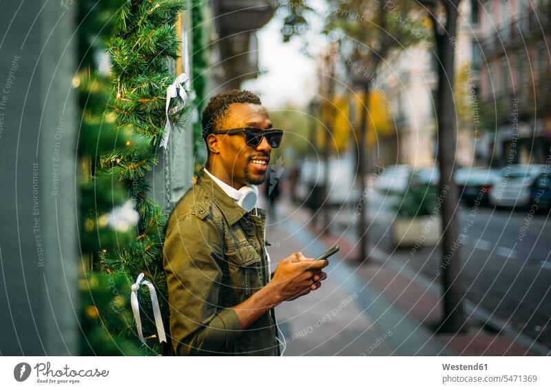Junger Mann trägt Sonnenbrille und benutzt ein Smartphone, während er in der Stadt auf dem Bürgersteig steht Farbaufnahme Farbe Farbfoto Farbphoto Spanien