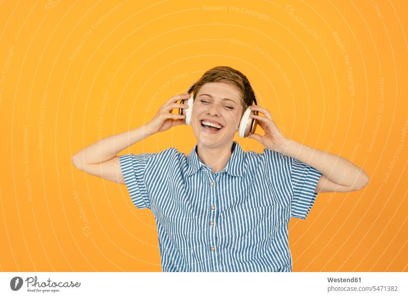 Porträt einer glücklichen Frau, die Musik mit orangem Hintergrund hört Leute Menschen People Person Personen kurzes Haar kurzes Haare Kurzhaarfrisur