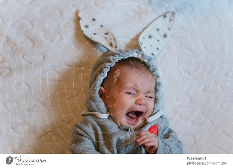 Porträt eines weinenden Mädchens in einem Kaninchen-Kapuzenpulli auf einer weißen Decke liegend Decken Betten rufen rufend Schrei schreiend gefühlvoll Emotionen