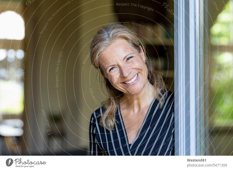 Porträt einer lächelnden reifen Frau, die an der geöffneten Terrassentür steht Leute Menschen People Person Personen Europäisch Kaukasier kaukasisch 1 Ein