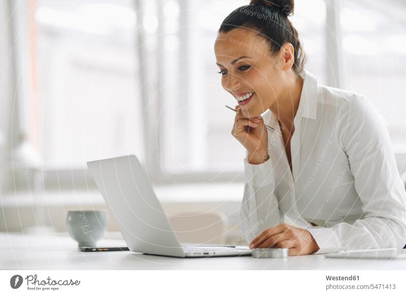 Lächelnde Geschäftsfrau mit Laptop auf dem Schreibtisch im Heimbüro Farbaufnahme Farbe Farbfoto Farbphoto Deutschland Innenaufnahme Innenaufnahmen innen drinnen