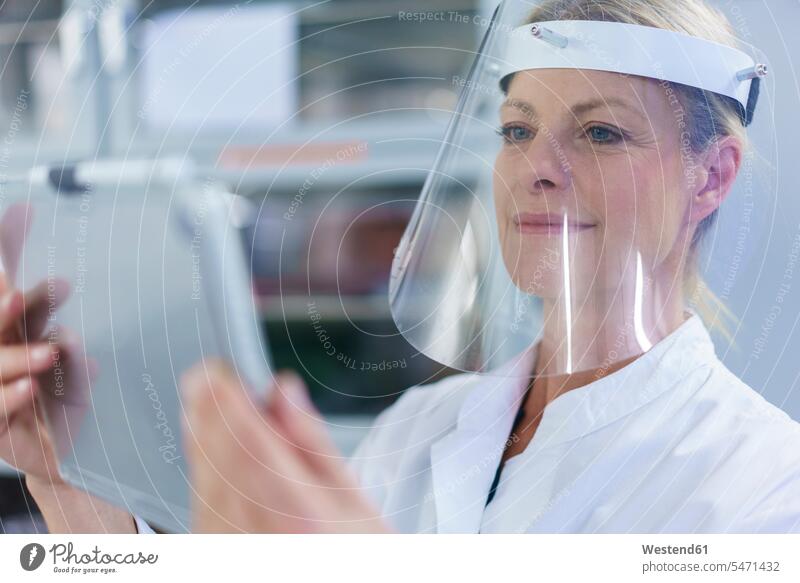 Ältere Wissenschaftlerin mit Gesichtsschutz bei der Verwendung eines digitalen Tabletts im Labor Farbaufnahme Farbe Farbfoto Farbphoto Innenaufnahme