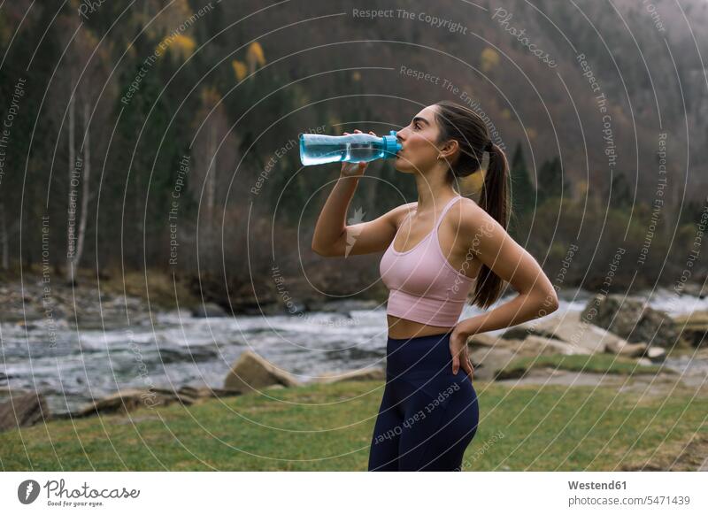 Erschöpfte junge Frau trinkt Wasser, während sie mit der Hand auf der Hüfte steht, Ordesa-Nationalpark, Huesca, Spanien Farbaufnahme Farbe Farbfoto Farbphoto