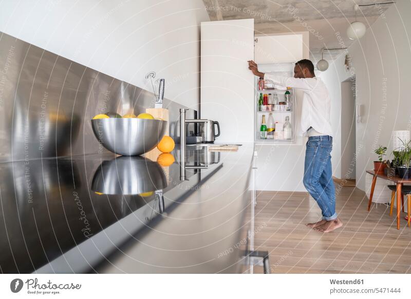 Mann steht in der Küche und schaut in den Kühlschrank Geräte Kühlschränke stehend daheim zu Hause auf geöffnet Muße Lifestyles Essen Essen und Trinken Food