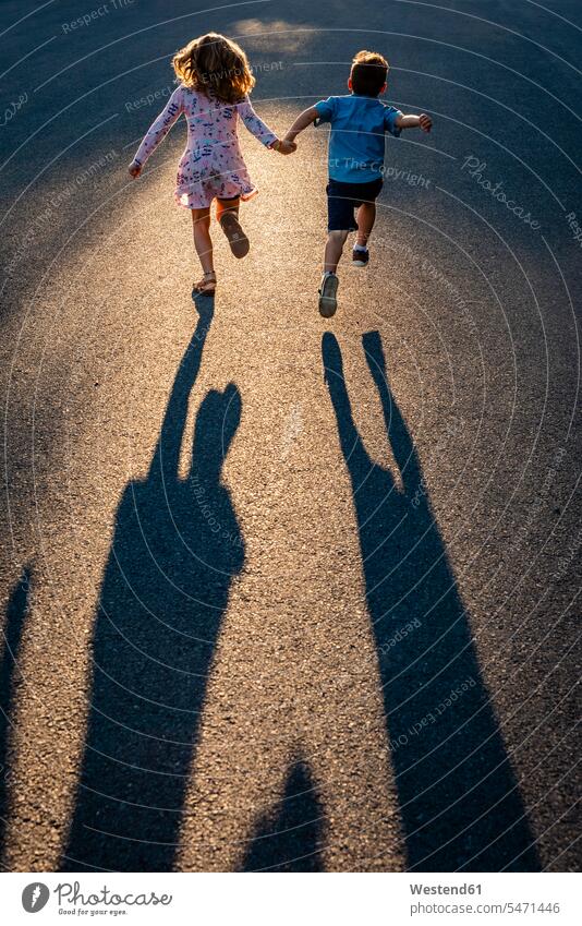 Rückansicht von Geschwistern, die sich an den Händen halten und auf der Straße laufen Farbaufnahme Farbe Farbfoto Farbphoto Kanada Canada Freizeitbeschäftigung