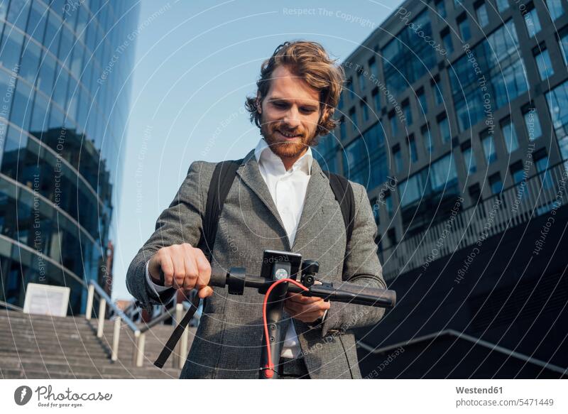 Männlicher Unternehmer benutzt Mobiltelefon, während er mit einem elektrischen Roller in der Innenstadt steht Farbaufnahme Farbe Farbfoto Farbphoto