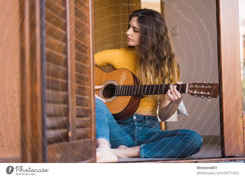 Junge Frau sitzt zu Hause auf dem Boden und spielt Gitarre sitzen sitzend spielen Gitarren Zuhause daheim weiblich Frauen Fußboden Fußboeden Fussboeden