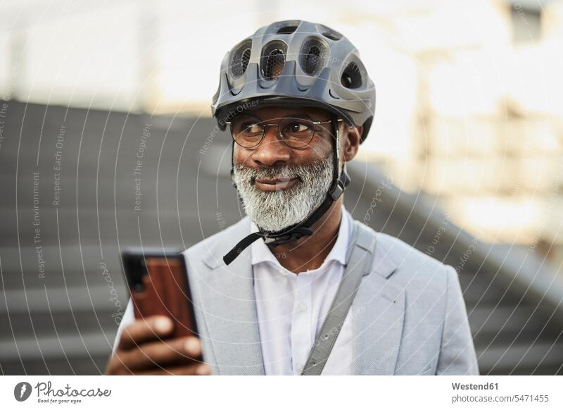 Porträt von lächelnden reifen Geschäftsmann mit Smartphone trägt Fahrradhelm und Brille geschäftlich Geschäftsleben Geschäftswelt Geschäftsperson
