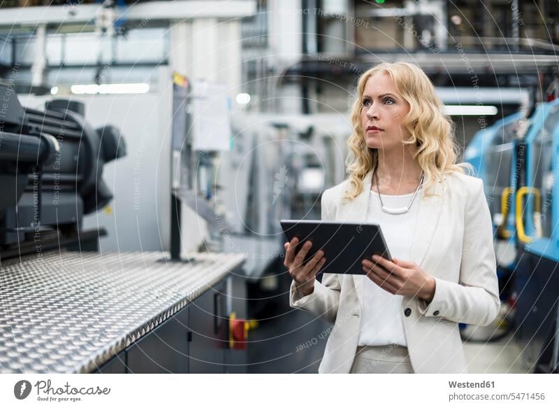 Frau mit Tablet an Maschine in Fabrikhalle schaut sich um weiblich Frauen Maschinen Industriehallen Fabrikhallen Fabriken Tablet Computer Tablet-PC Tablet PC