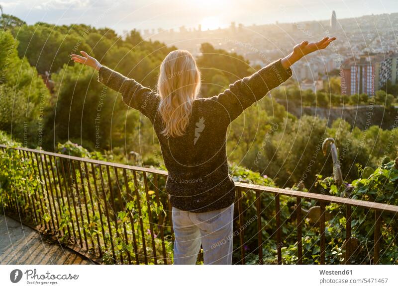 Rückansicht einer sorglosen jungen Frau, die bei Sonnenaufgang über der Stadt steht, Barcelona, Spanien Leute Menschen People Person Personen Europäisch